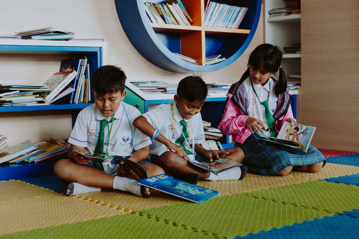 Three children in school uniform reading picture books on the colourful library floor