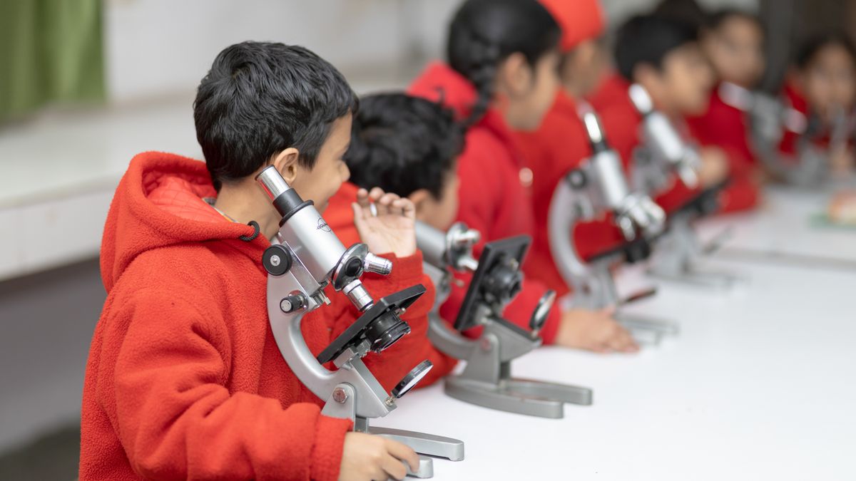 Young students in red uniforms looking through microscopes in the science lab